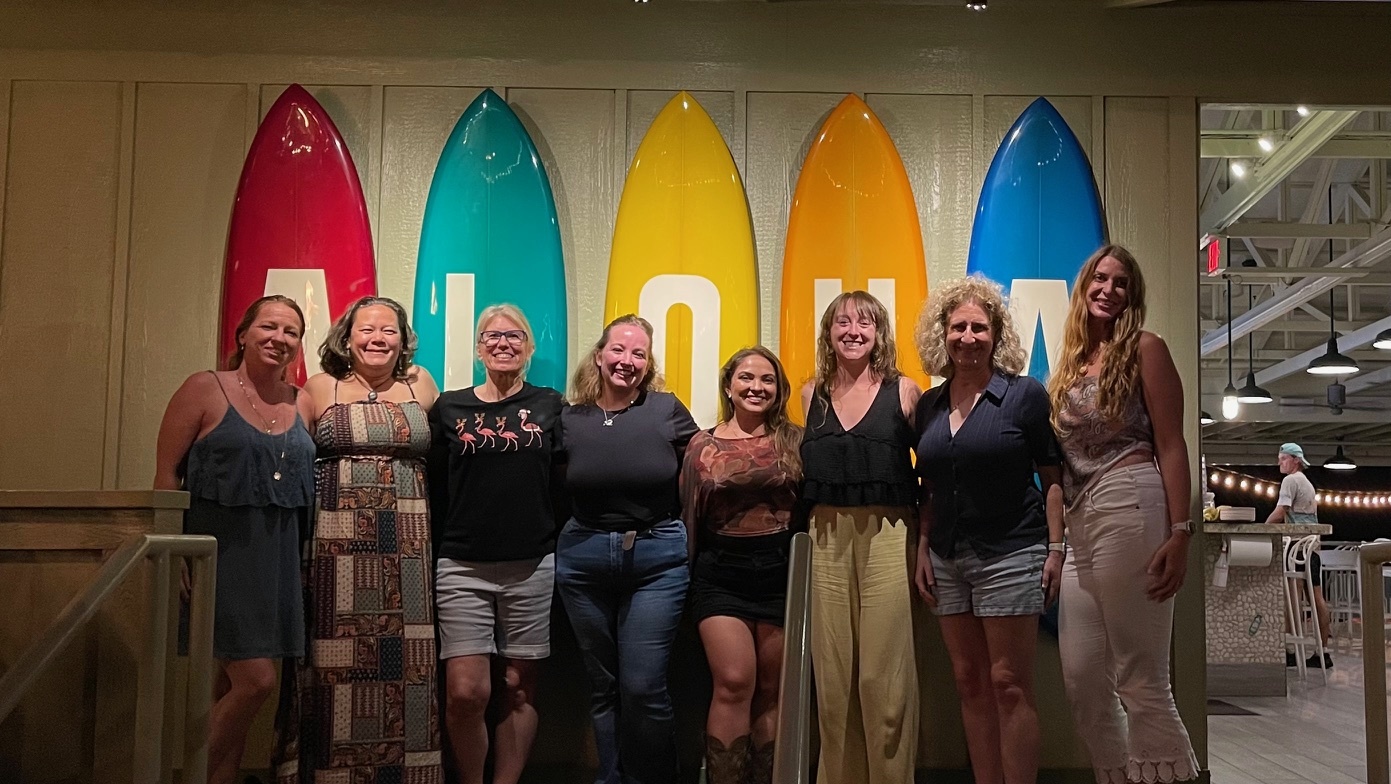 MRA Christmas Dinner. The crew standing in front of multi-colored surfboards spelling "Aloha". From Left to Right: Ty, Rhiannon, Kerstin, Savannah, Juli, Ashley, Martina, and Ari