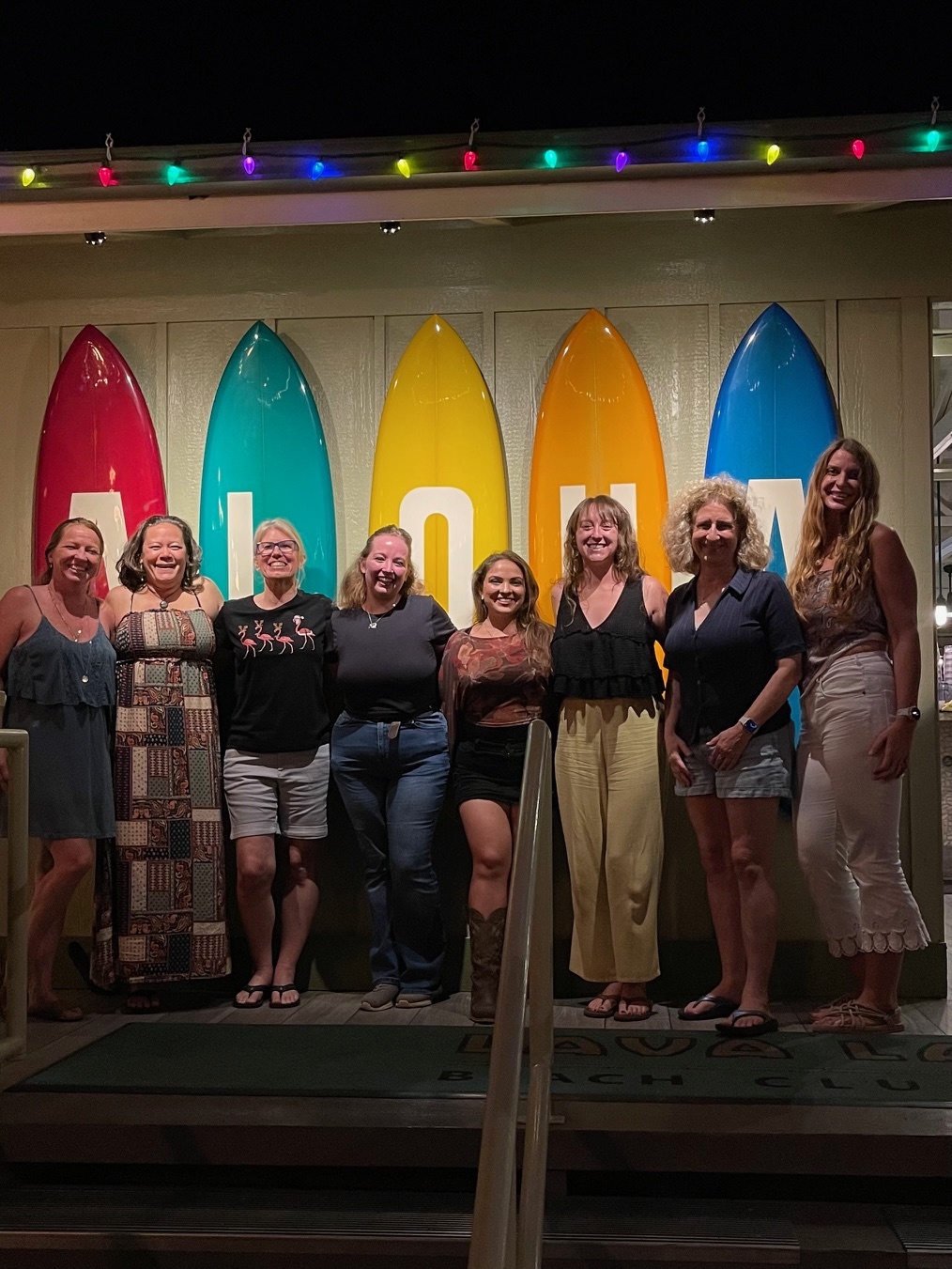MRA Christmas Dinner. The crew standing in front of multi-colored surfboards spelling "Aloha". From Left to Right: Ty, Rhiannon, Kerstin, Savannah, Juli, Ashley, Martina, and Ari