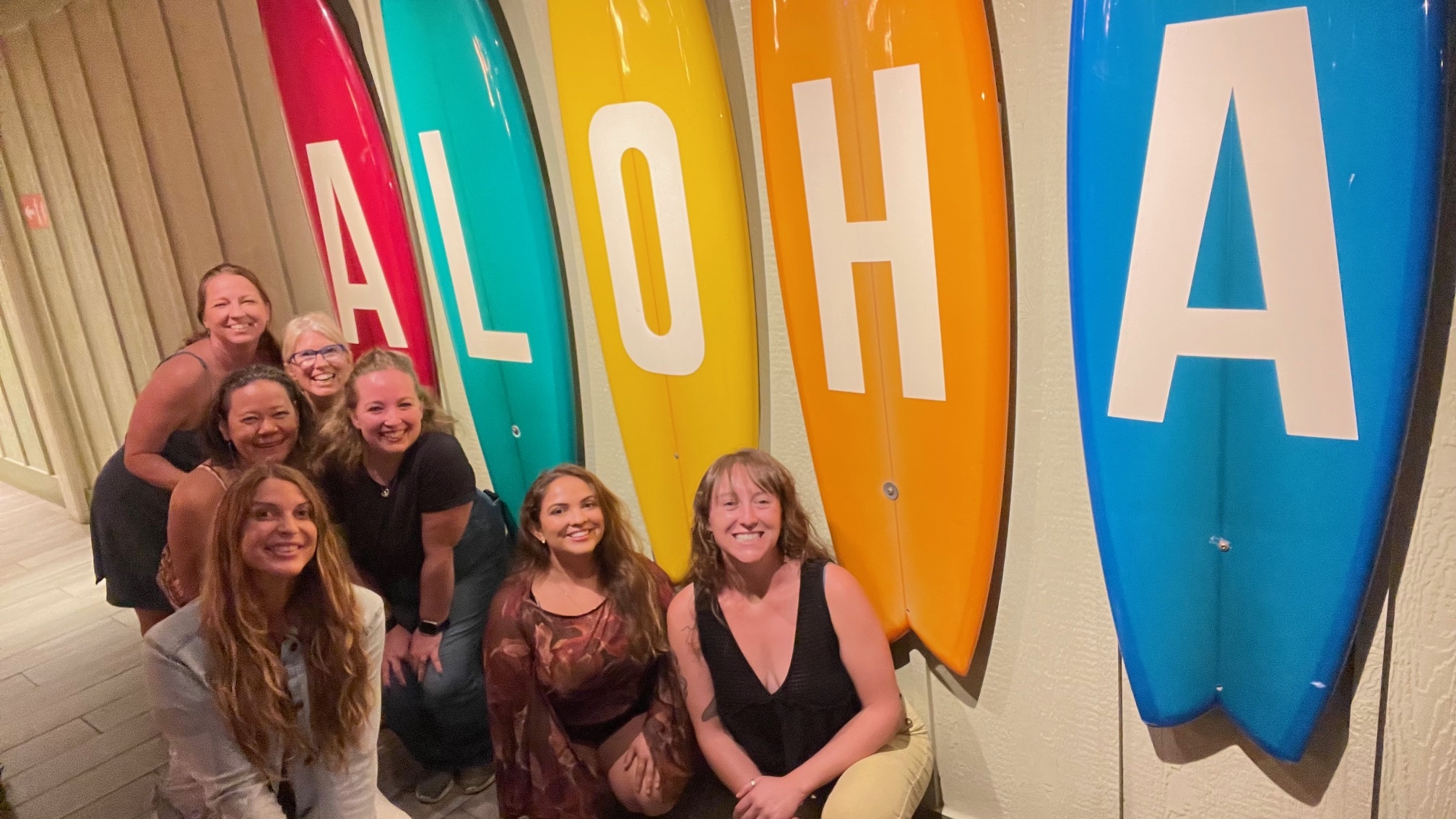 MRA Christmas Dinner. The crew standing next to multi-colored surfboards spelling "Aloha". From back to front: Ty, Kerstin, Rhiannon, Savannah, Ari, Juli, and Ashley